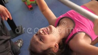<strong>儿童表演</strong>板凳压躺与教练。 女孩加强了手的肌肉。 健身俱乐部的青少年